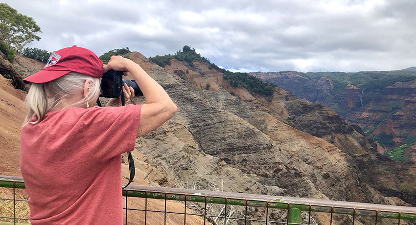 A senior citizen points her camera at the canyon she's visiting in Hawaii.