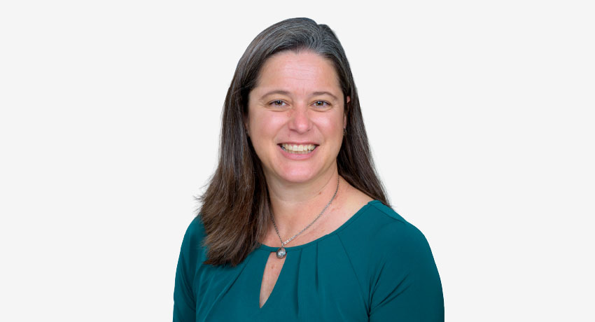 Formal head-and-shoulders studio portrait of a woman with long brown hair wearing a teal top and a necklace against a white background