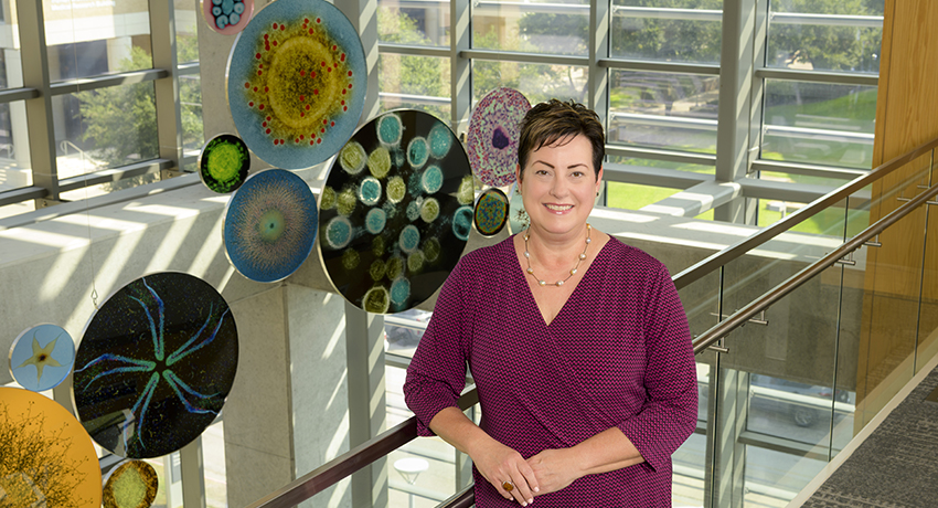Kristen Starnes-Ott, wearing a wine-colored dress, poses in front of an art installation of colorful round glass pieces.