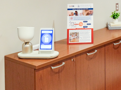 Five people stand together in an office setting near a cabinet and coffee table. A wall-mounted display screen and seating area are visible in the background.